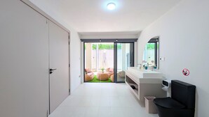 Une salle de bain moderne avec un grand miroir, deux lavabos et des toilettes. Une porte coulissante en verre donne accès à un espace extérieur aménagé avec une chaise et une petite table.