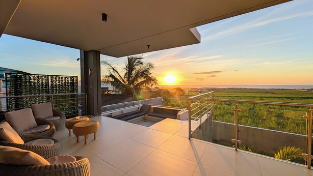 Un balcon offrant une vue sur le coucher de soleil au-dessus d’un paysage verdoyant.