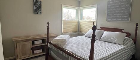 A bedroom with a four-poster bed, a ceiling fan, a window with blinds, and motivational posters on the walls.