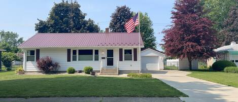 A single-story house with a red roof, a front porch, and an American flag.