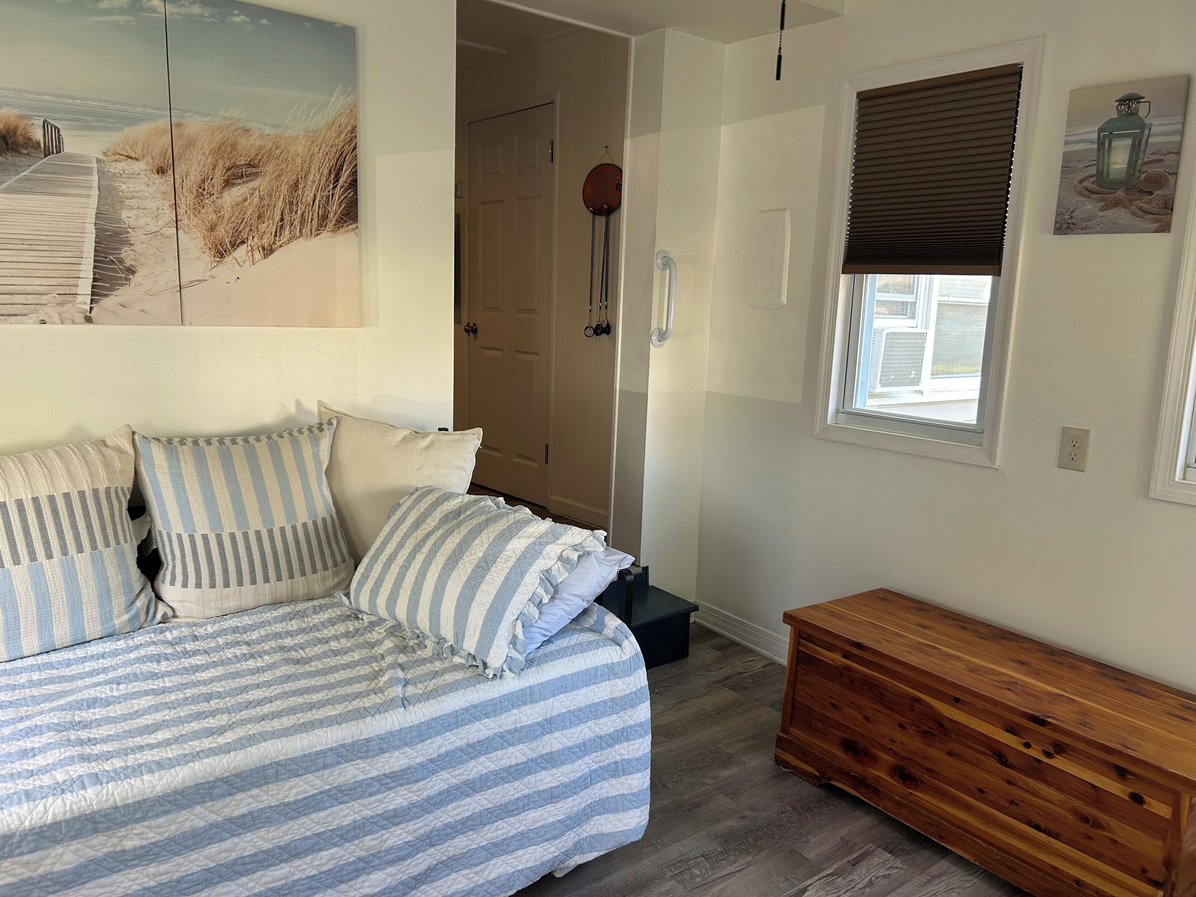 Ein Schlafzimmer mit einem gestreiften Bett, einer hölzernen Bank, einer Tür und einem Fenster mit Jalousien.