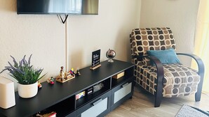 A living room with a flat-screen TV mounted on the wall, a black entertainment unit with drawers, a patterned armchair, and a decorative wall piece. - 2-bedroom apartment next to Brave's Stadium (Smyrna)