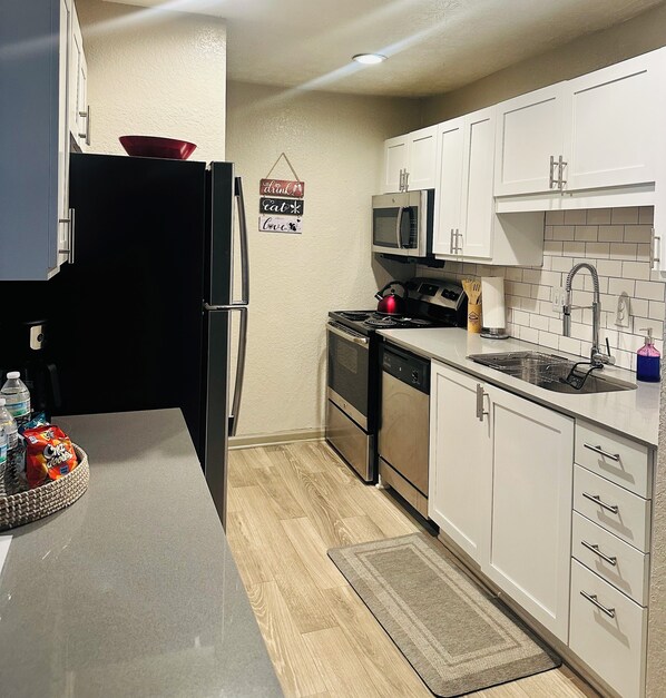 A modern kitchen with white cabinets, a stainless steel refrigerator, a microwave, a stove, and a dishwasher.