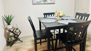 A dining area with a table set for four, surrounded by chairs, a potted plant, and a framed floral painting on the wall. - 2-bedroom apartment next to Brave's Stadium (Smyrna)