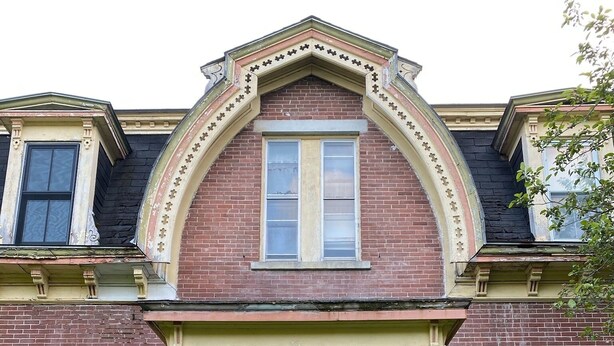 A two-story brick house with a black front door, a small porch with a light fixture, and a window above the door.