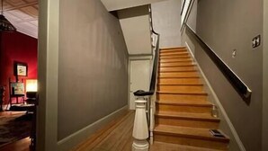 A staircase with wooden steps and a handrail, leading to a landing with a white wall and a door.
