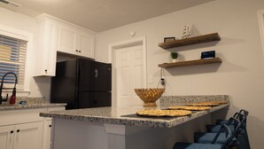 A kitchen with white cabinets, a black refrigerator, granite countertops, a woven basket, and blue chairs. - Beautiful, modern furnished 3-bedroom, 2-bathroom cottage near attractions. (Portsmouth)