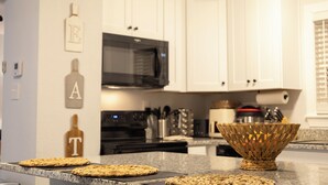 A kitchen with white cabinets, a microwave, and a woven basket on the counter. - Beautiful, modern furnished 3-bedroom, 2-bathroom cottage near attractions. (Portsmouth)