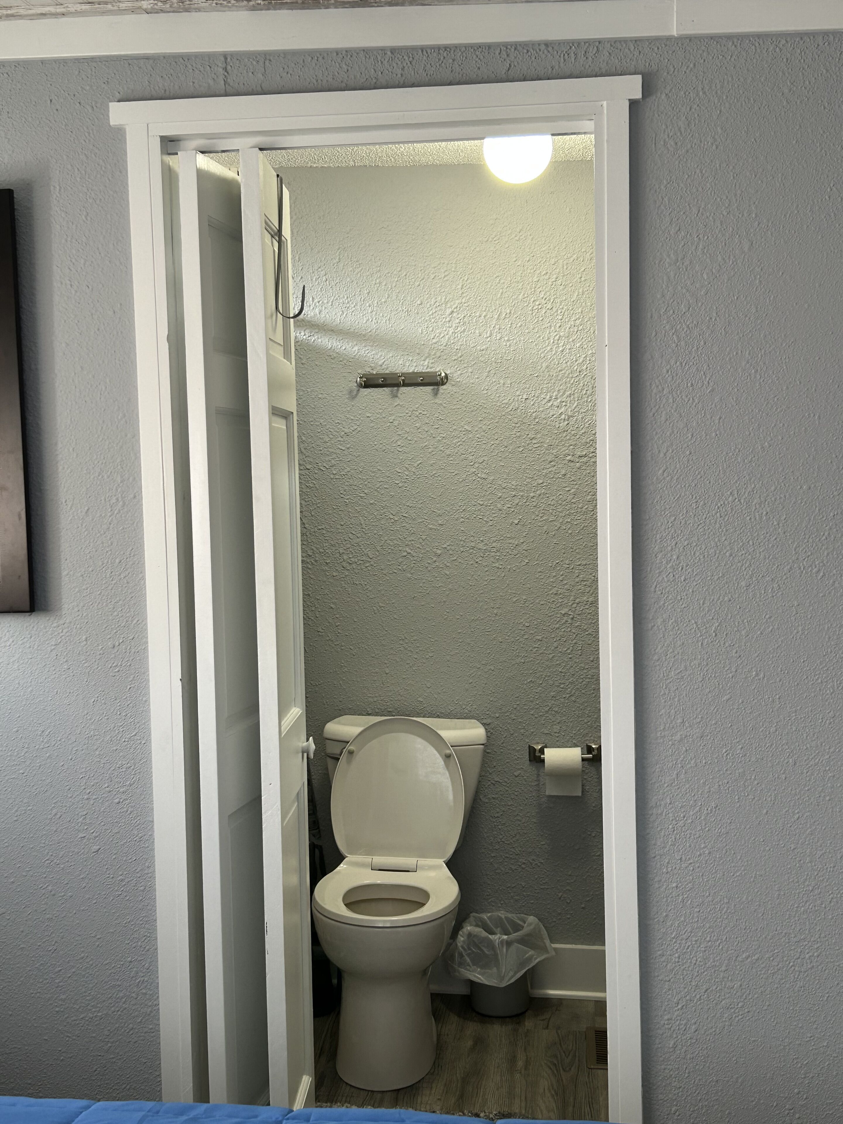Un baño pequeño y estrecho con inodoro, un cubo de basura y zona de ducha.