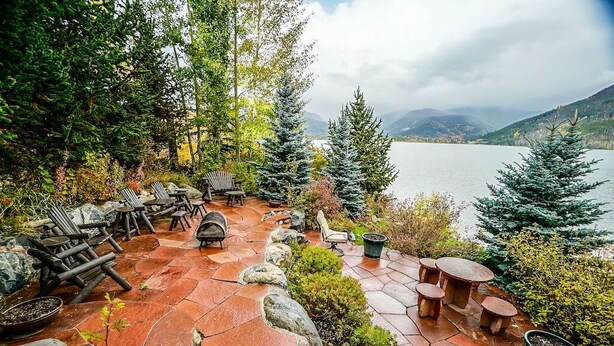Eine Terrasse mit Sitzgelegenheiten, Steinböden und Blick auf einen See und Berge.