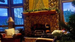 Ein gemütliches Interieur mit Kamin aus Stein, Ledermöbeln und einem großen Fenster mit Blick auf Bäume.