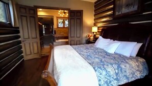 Ein Schlafzimmer mit einem großen Bett, Holzwandverkleidung, einem Nachttisch mit Lampe und Blick ins Freie durch ein Fenster.
