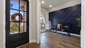 Un interior moderno con una puerta negra, piso de madera, un escritorio con una silla y una pared oscura con un motivo geométrico.