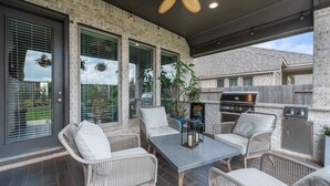 Un patio exterior con mobiliario de mimbre, una mesa y una zona de barbacoa.