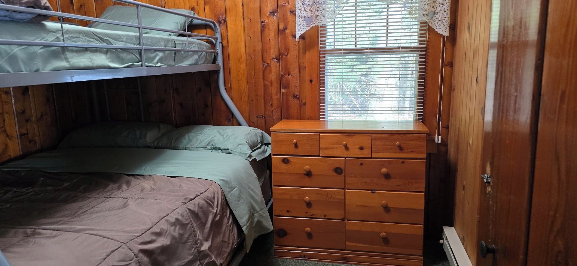 A bunk bed with a window above, wooden walls, and a dresser with drawers.