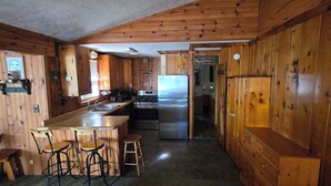 A wooden cabin interior with a kitchen area, bar stools, and a refrigerator. - Family and pet friendly, waterfront cabin on Lost Lake, with private dock (Saint Germain)