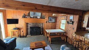 A cozy cabin interior with a fireplace, wooden walls, a flat-screen TV, a chessboard, and a bar area. - Family and pet friendly, waterfront cabin on Lost Lake, with private dock (Saint Germain)