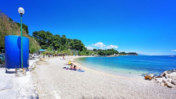 A beach with clear blue water, a few people sunbathing, and a blue lamp post. - Adriatic Retreat Meje 4 min to the beach (Split)