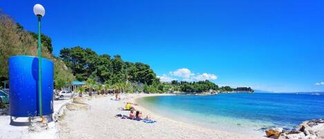 Une plage avec une eau d’un bleu limpide, quelques personnes qui prennent un bain de soleil et un lampadaire bleu.