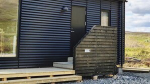 A modern building with a metal exterior, a wooden staircase, and a gravel ground. - Cosy Northern Ligths Cabin with hot tub and magical views on the Golden Circle (Grímsnes- og Grafningshreppur)
