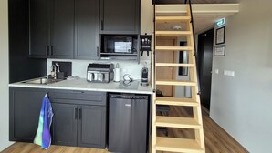 A modern kitchen with black cabinets, a microwave, a toaster, and a dishwasher. There is a wooden ladder leading to a lofted area. - Cosy Northern Ligths Cabin with hot tub and magical views on the Golden Circle (Grímsnes- og Grafningshreppur)
