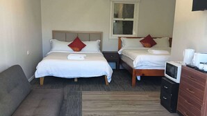 Habitación de hotel con dos camas, un sofá, un televisor y piso de madera.