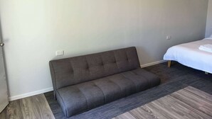 Una habitación moderna con un sofá gris, una cama con ropa de cama blanca y una alfombra gris.