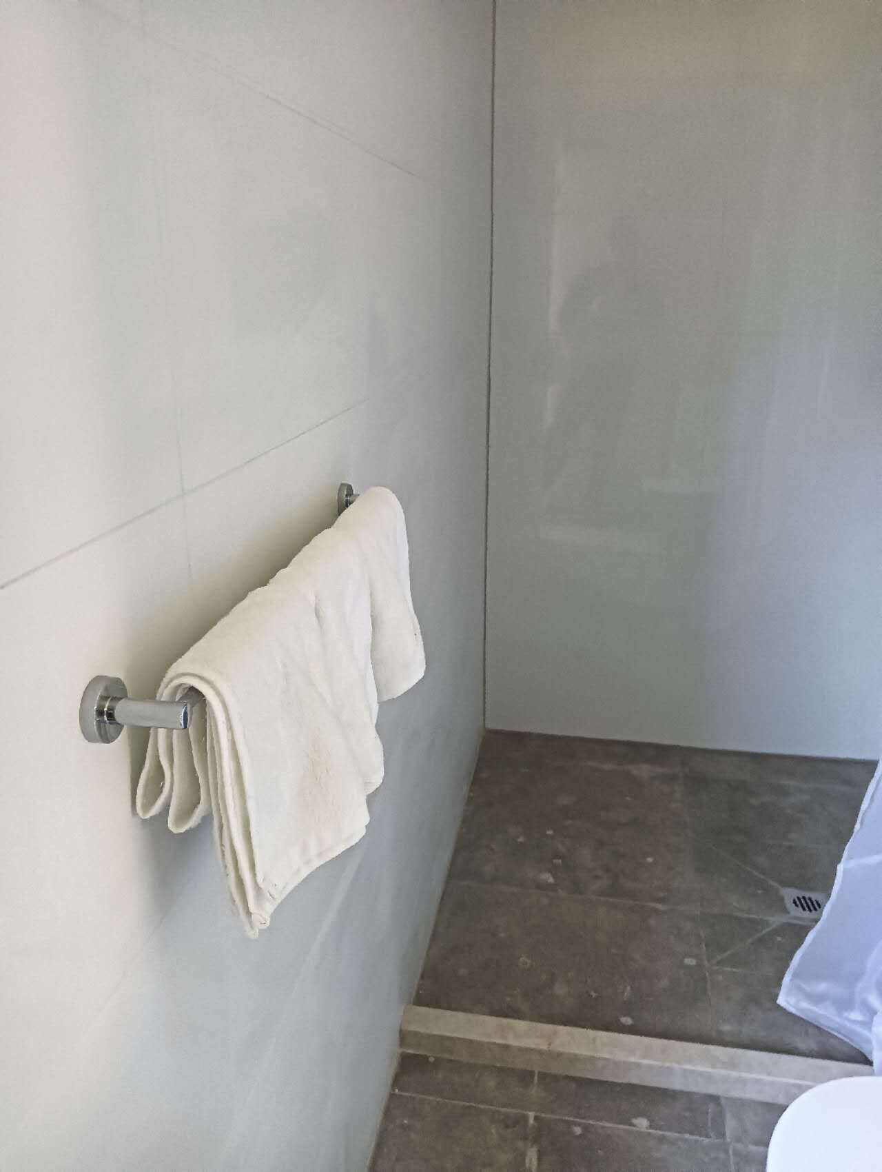 Een badkamer met een handdoekhouder, een opgevouwen handdoek, betegelde muren en een douchegedeelte.