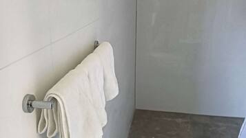 Een badkamer met een handdoekhouder, een opgevouwen handdoek, betegelde muren en een douchegedeelte.