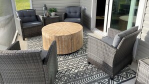Un patio techado con mobiliario de mimbre, una mesa redonda de madera y un tapete estampado.