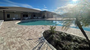 Zona de piscina con patio de ladrillo, sillas de descanso y un área de estar cubierta.