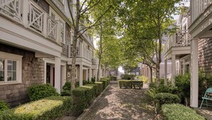 A narrow, tree-lined street with uniform buildings, a gravel path, and a bench. - Arcade, Family + Dog Friendly, Seabrook Town Center Home, 5min. walk to beach (Pacific Beach)