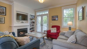 A living room with a fireplace, a television, a red armchair, and a grey sofa. - Arcade, Family + Dog Friendly, Seabrook Town Center Home, 5min. walk to beach (Pacific Beach)