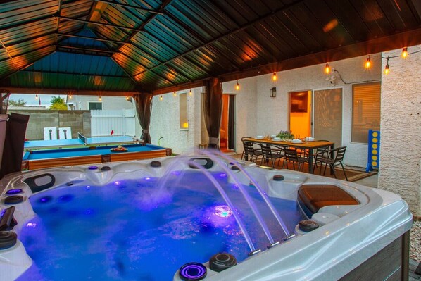 A hot tub area with a pool table, a dining table, and a covered patio.