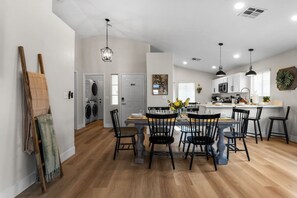 Une cuisine moderne avec des meubles blancs, un coin repas avec des chaises noires et une buanderie équipée d’un lave-linge.
