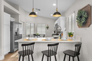 A modern kitchen with a central island, black chairs, and pendant lighting.
