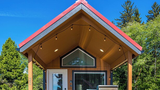 A covered outdoor area with a wooden deck, a door, and a small enclosed space with a window. - Rainforest Retreat Tiny Home: Fishing Cabin (Forks)