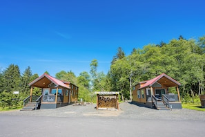 Duas cabanas de madeira com telhados vermelhos, um caminho de acesso de cascalho e uma pilha de lenha no centro.