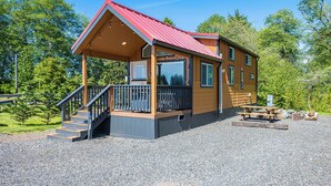 A cabin with a red roof, a porch with steps, and a gravel ground. - Rainforest Retreat Tiny Home: Fishing Cabin (Forks)