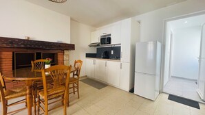 A compact kitchen with white cabinets, a microwave, and a refrigerator. There is a dining table with chairs and a hanging light fixture.