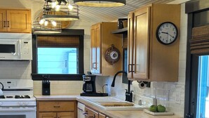 Una cocina con armarios de madera, microondas, estufa, cafetera y un reloj en la pared.