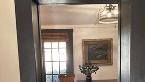 Un área de comedor con una mesa de madera, una silla, un florero con flores, un cuadro en la pared y una ventana con persianas.