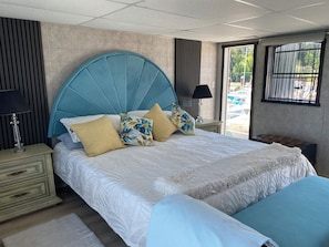 A double bed with a large blue headboard, two bedside tables with lamps, a bench, and a view of the outdoors through a window. - "Flagship 1" Live-Aboard BNB: Paddle Boards, Kayaks, Crabbing, and More (Willis Point)
