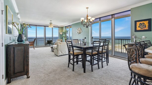 Ein geräumiger Essbereich mit großem Tisch und Stühlen, einer Chandelierleuchtre und Blick auf das Meer durch große Fenster.