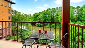 A balcony with a table and chairs overlooking a river and forest.