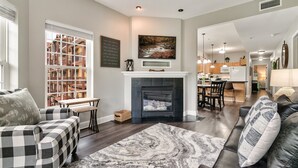 A modern living room with a fireplace, a dining area, and a kitchen in the background.