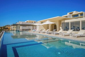 A modern hotel with a swimming pool, sun loungers, and umbrellas.