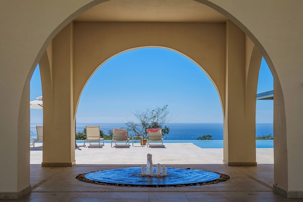 An arched outdoor area with a pool, chairs, and a view of the sea.