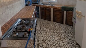 A kitchen with a gas stove, wooden cabinets, a window, and patterned floor tiles.