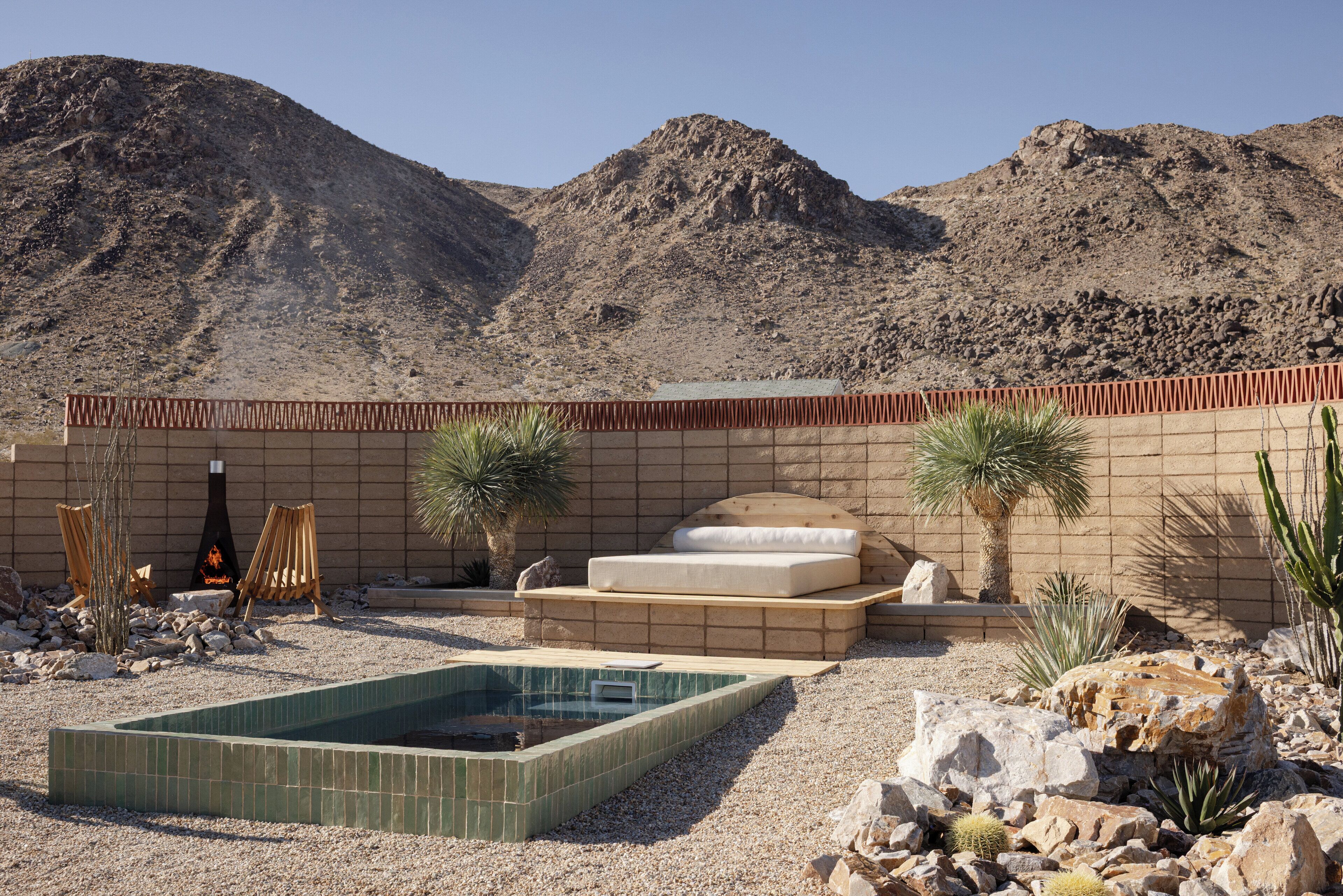 Un paysage désertique avec une piscine, un mur de briques et un lit donnant sur les montagnes.